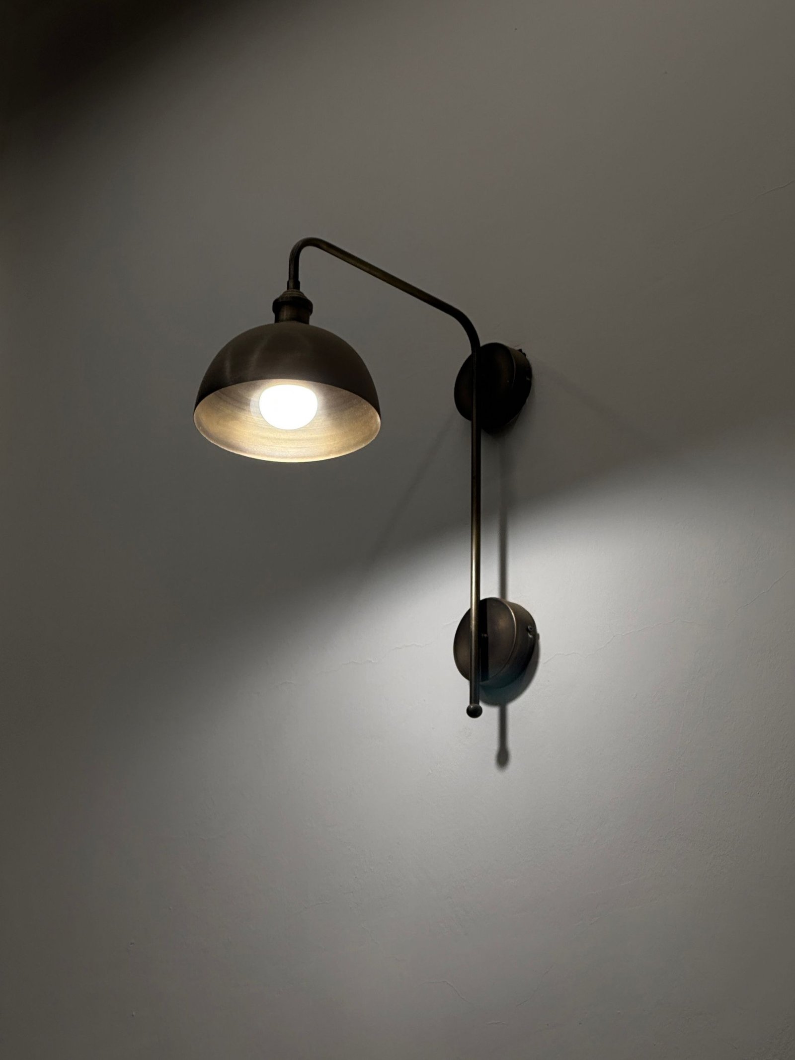 A classic brass wall sconce with a glowing light bulb casting a warm glow.