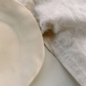 Close-up of a ceramic plate on crumpled linen cloth, showcasing minimalist design.