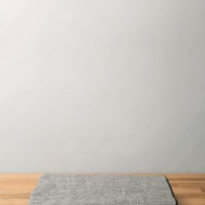 Minimalist image of a folded gray wool blanket on a wooden table against a neutral backdrop.