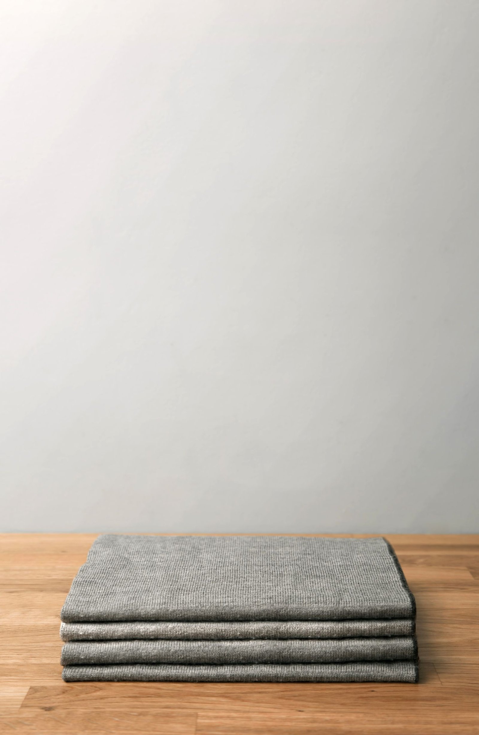 Minimalist image of a folded gray wool blanket on a wooden table against a neutral backdrop.