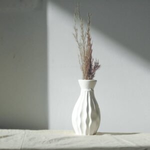 Minimalist white vase with decorative dried grass on a gray background, showcasing simplicity and elegance.