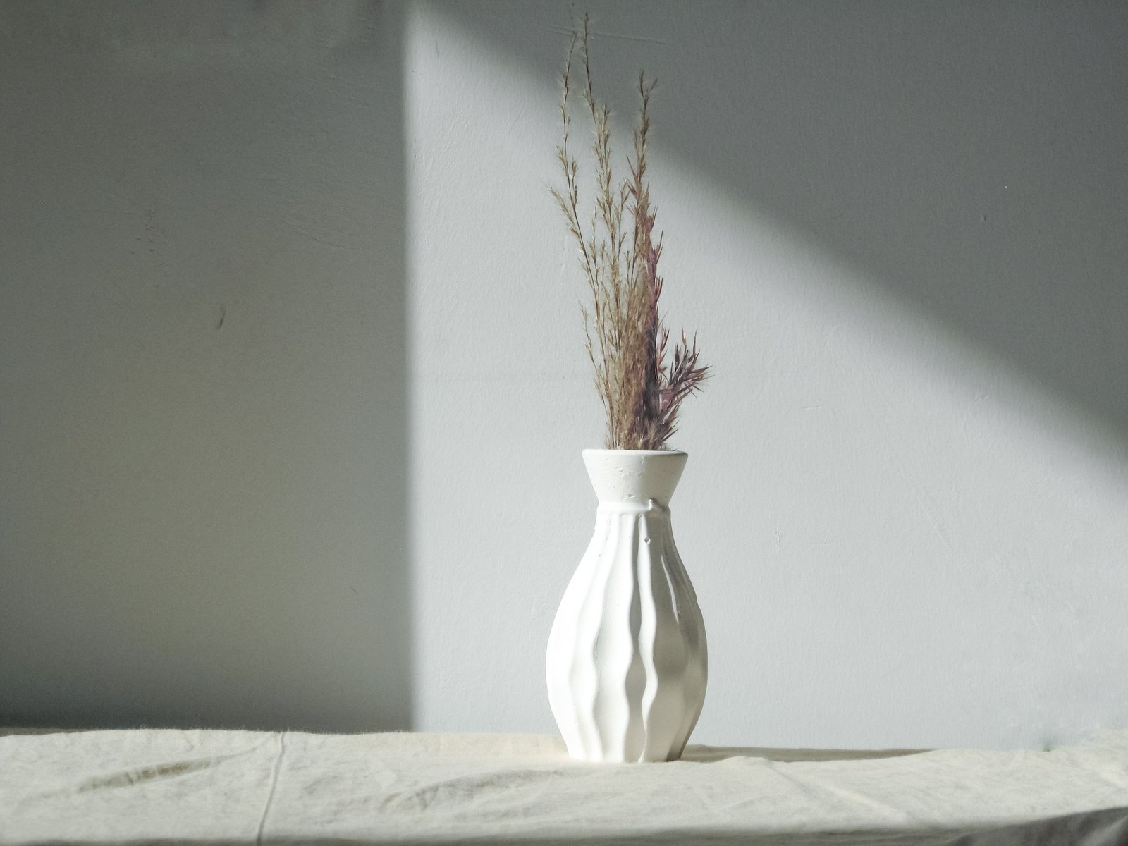 Minimalist white vase with decorative dried grass on a gray background, showcasing simplicity and elegance.