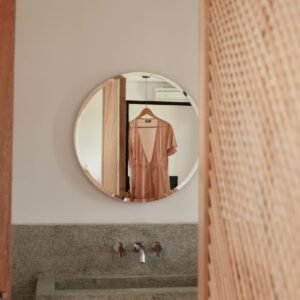 Stylish dress hangs reflected in a round mirror, enhancing a modern bathroom's minimalist decor.
