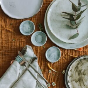 Top view of a rustic table setting with ceramic plates, cutlery, and fresh greenery.
